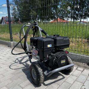 Czarna myjka cisnieniowa na tle kostki i ogrodzenia